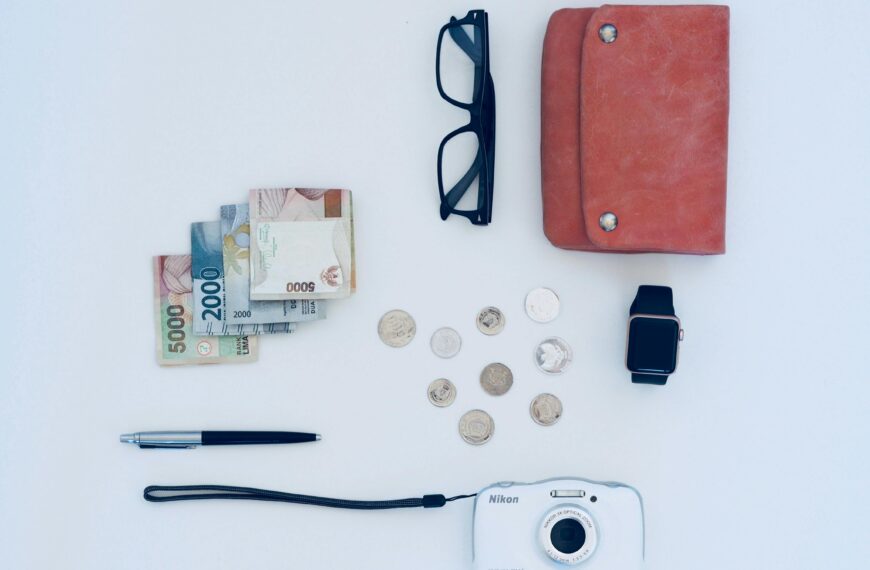 Flat lay of everyday items including currency, coins, wallet, and gadgets, all on a white background.