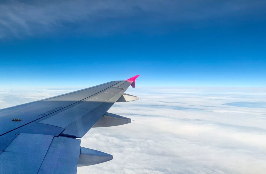 Aerial view of an airplane wing above clouds with clear blue sky, offering serene travel vibes.