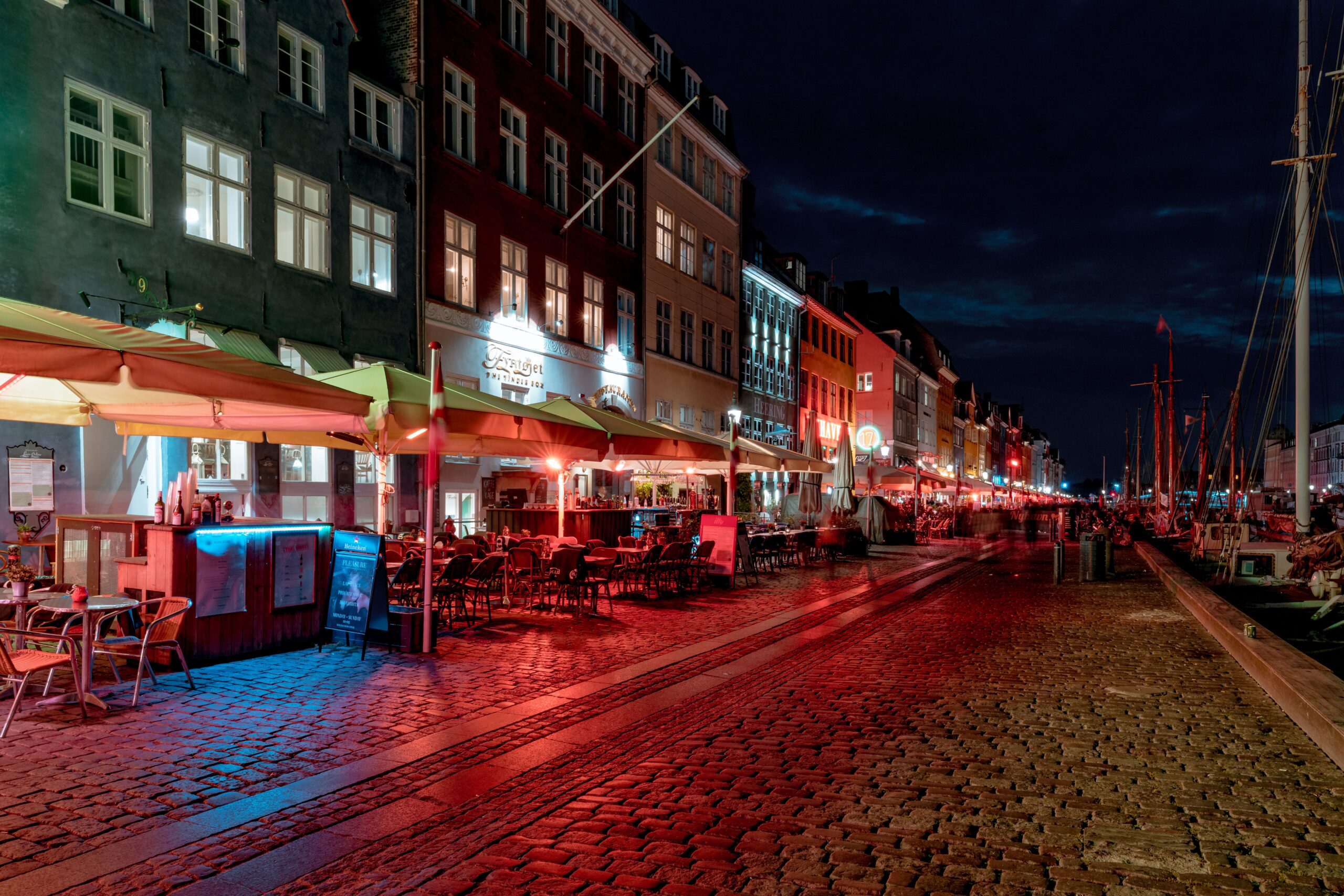 Explore the vibrant nightlife of Nyhavn with illuminated restaurants along the cobblestone street.