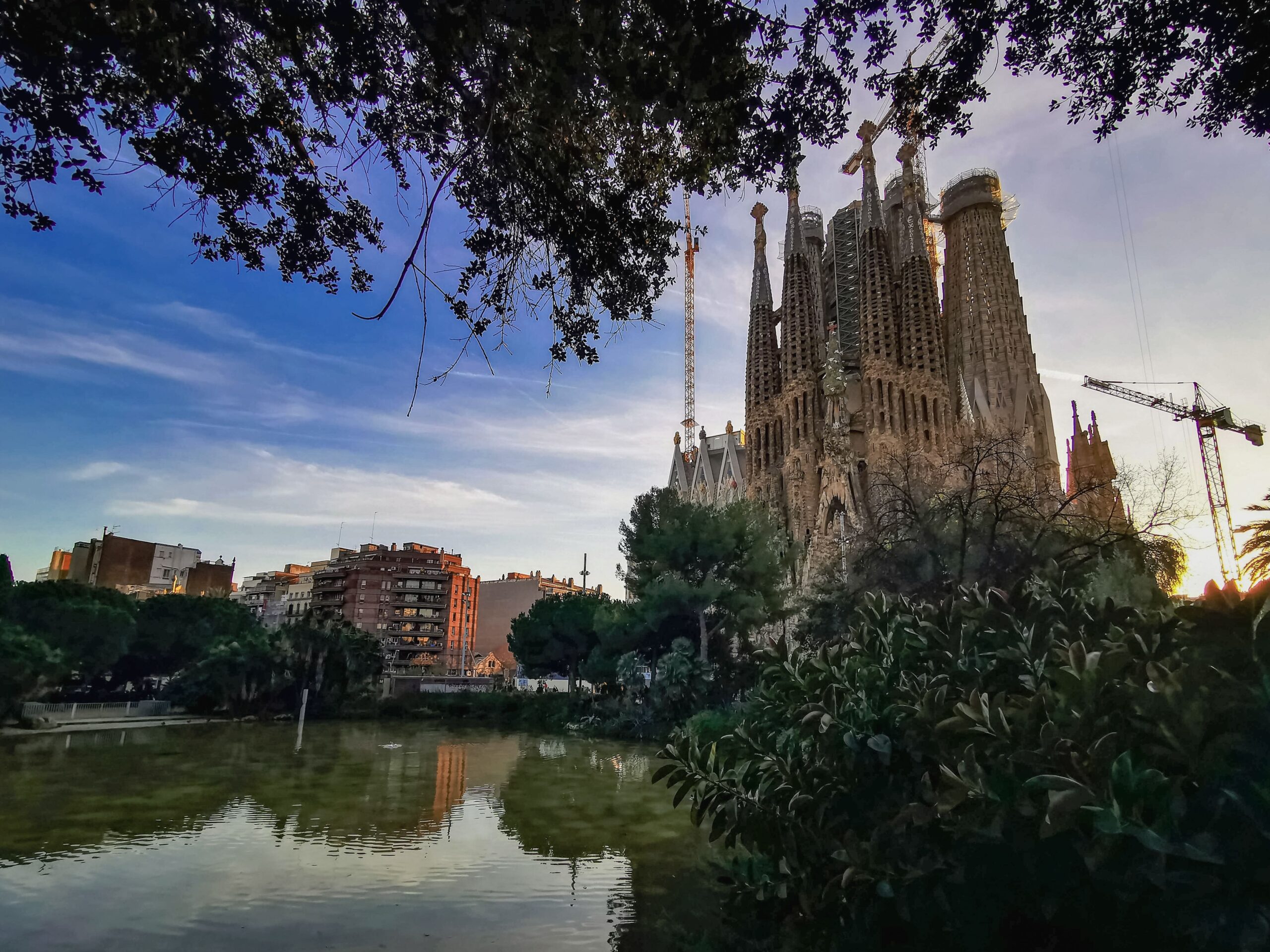 Capture of the iconic Sagrada Familia in Barcelona at sunset with reflections on a nearby pond.