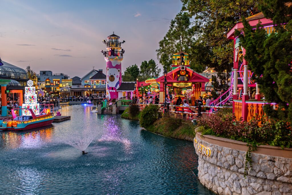 Vibrant amusement park canal scene at twilight with colorful lights and attractions.