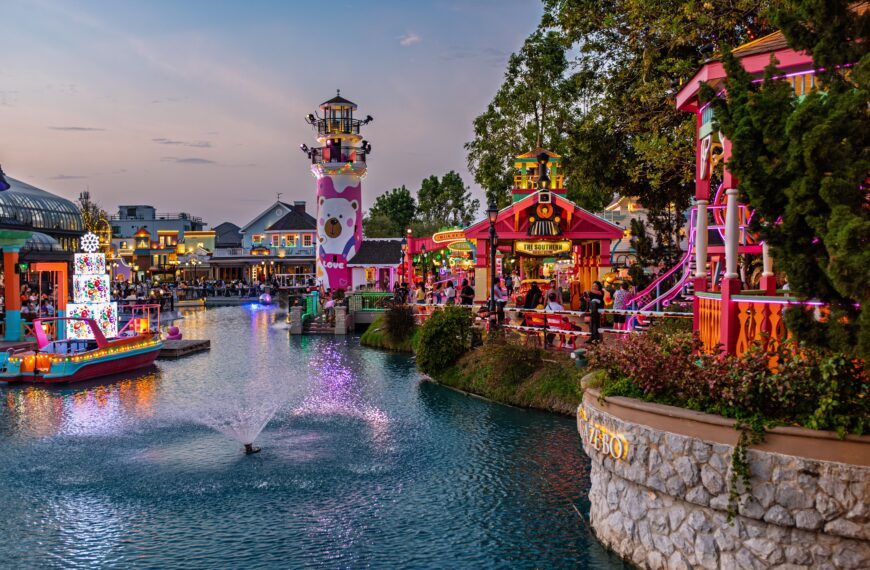 Vibrant amusement park canal scene at twilight with colorful lights and attractions.