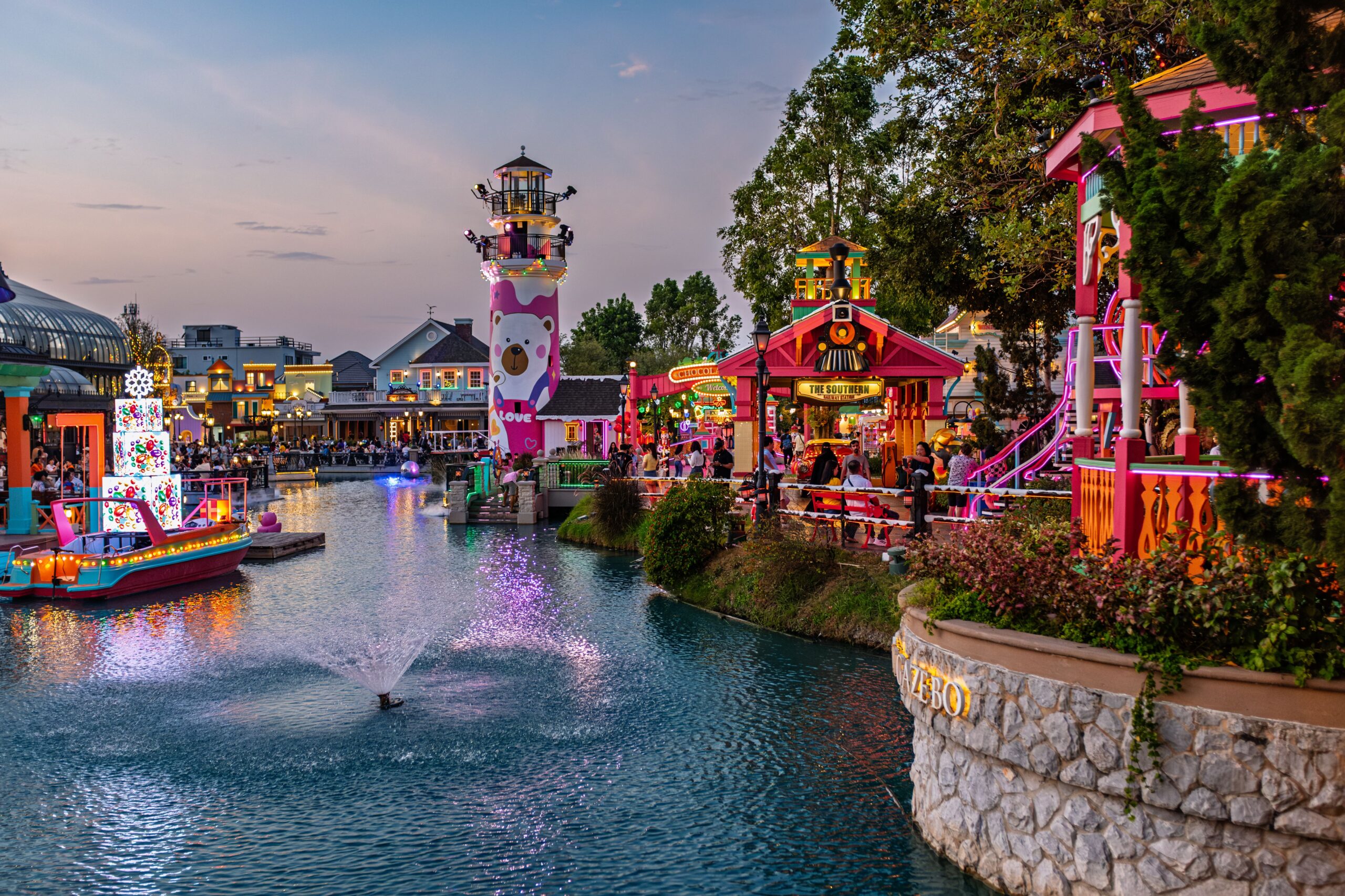 Vibrant amusement park canal scene at twilight with colorful lights and attractions.
