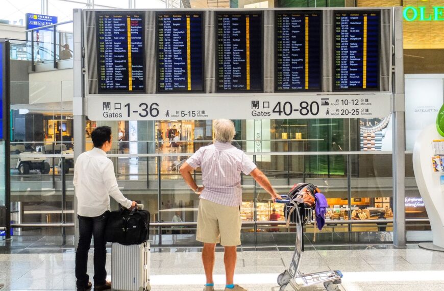Passengers review flight information on a digital board in Hong Kong airport terminal.