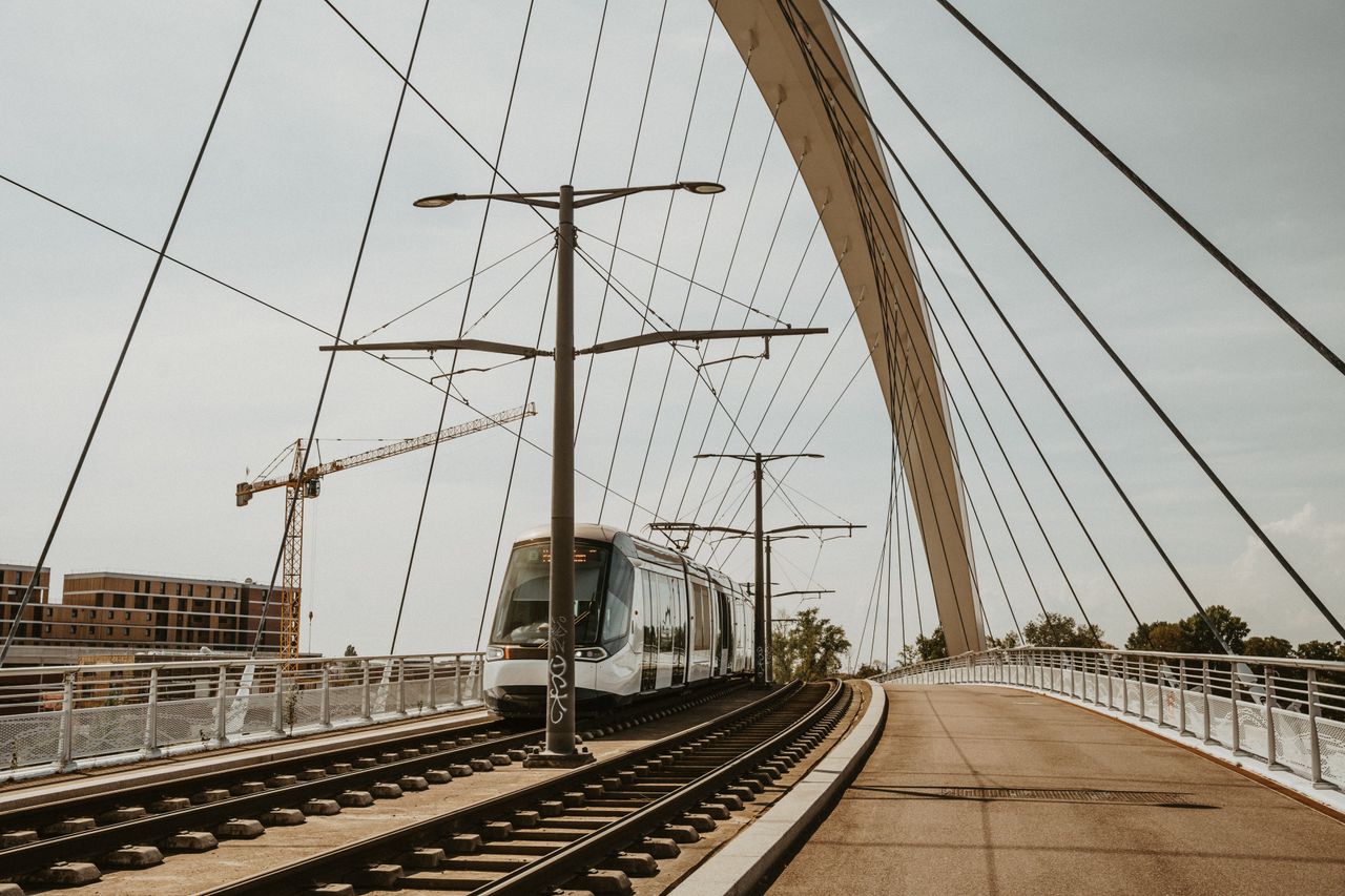 A sleek tram traverses a contemporary cable-stayed bridge in an urban setting.