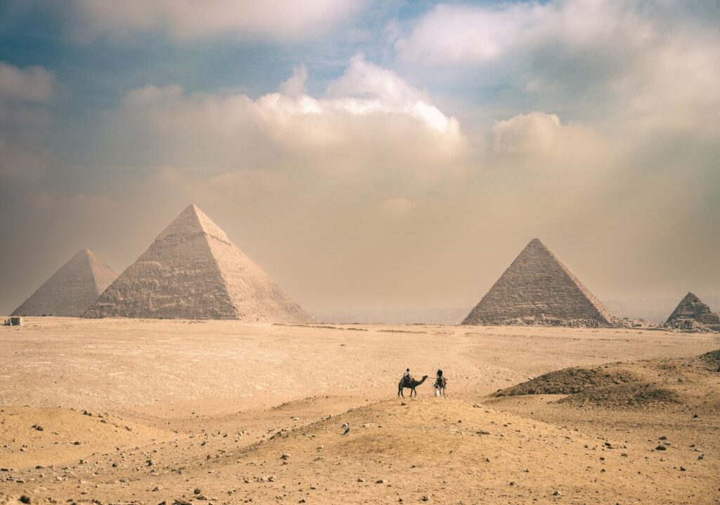 Oplev de majestætiske pyramider i Giza under en solrig himmel med rejsende på kameler i det fjerne.