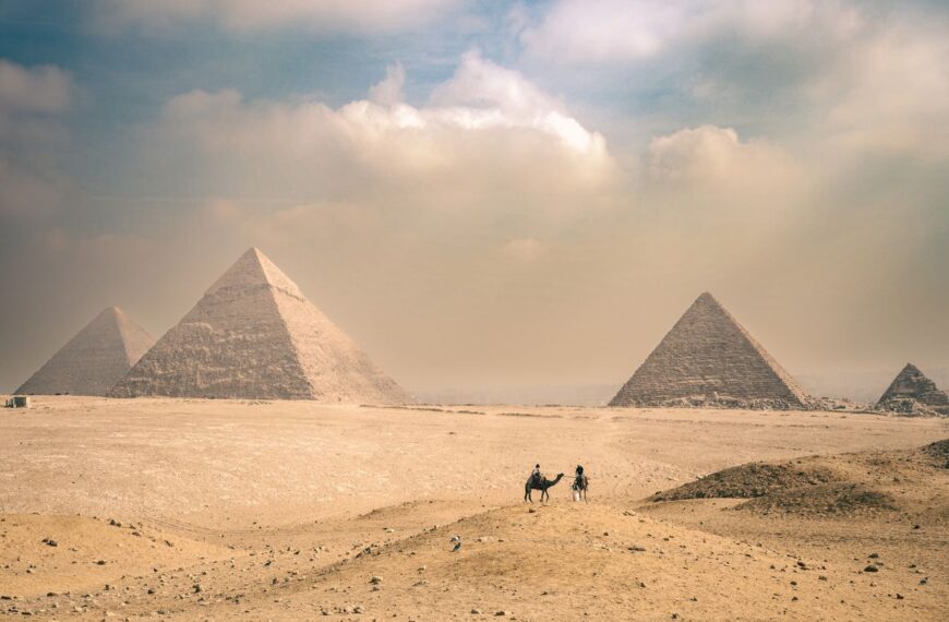 Explore the majestic Pyramids of Giza under a sunny sky with distant travelers on camels.