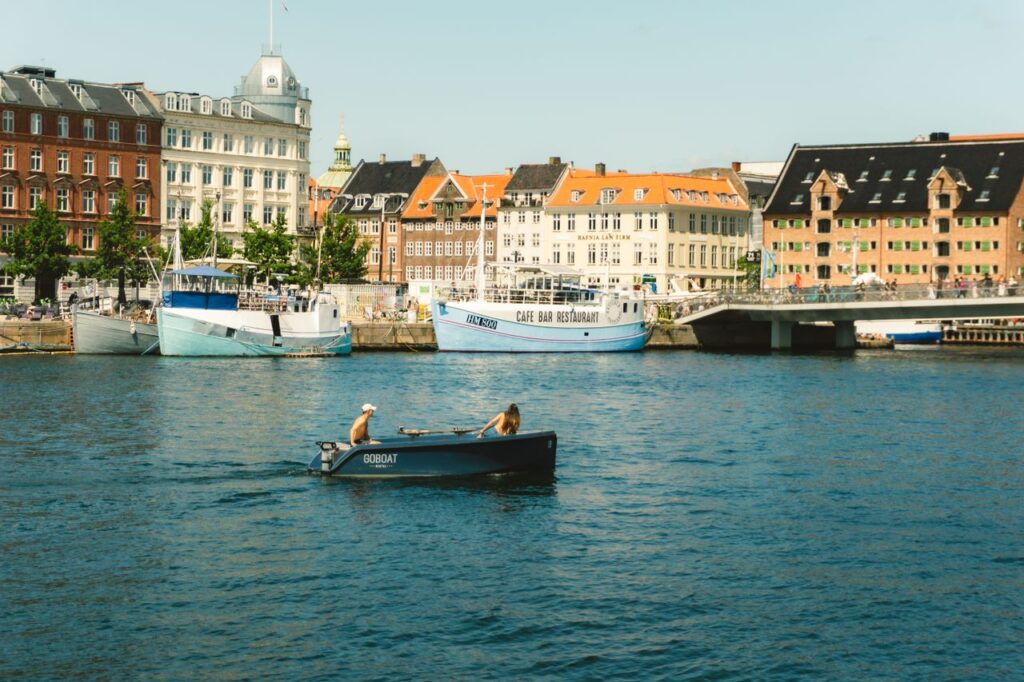 Afslappende kanalscene i København med mennesker i en robåd, der nyder en solrig dag.
