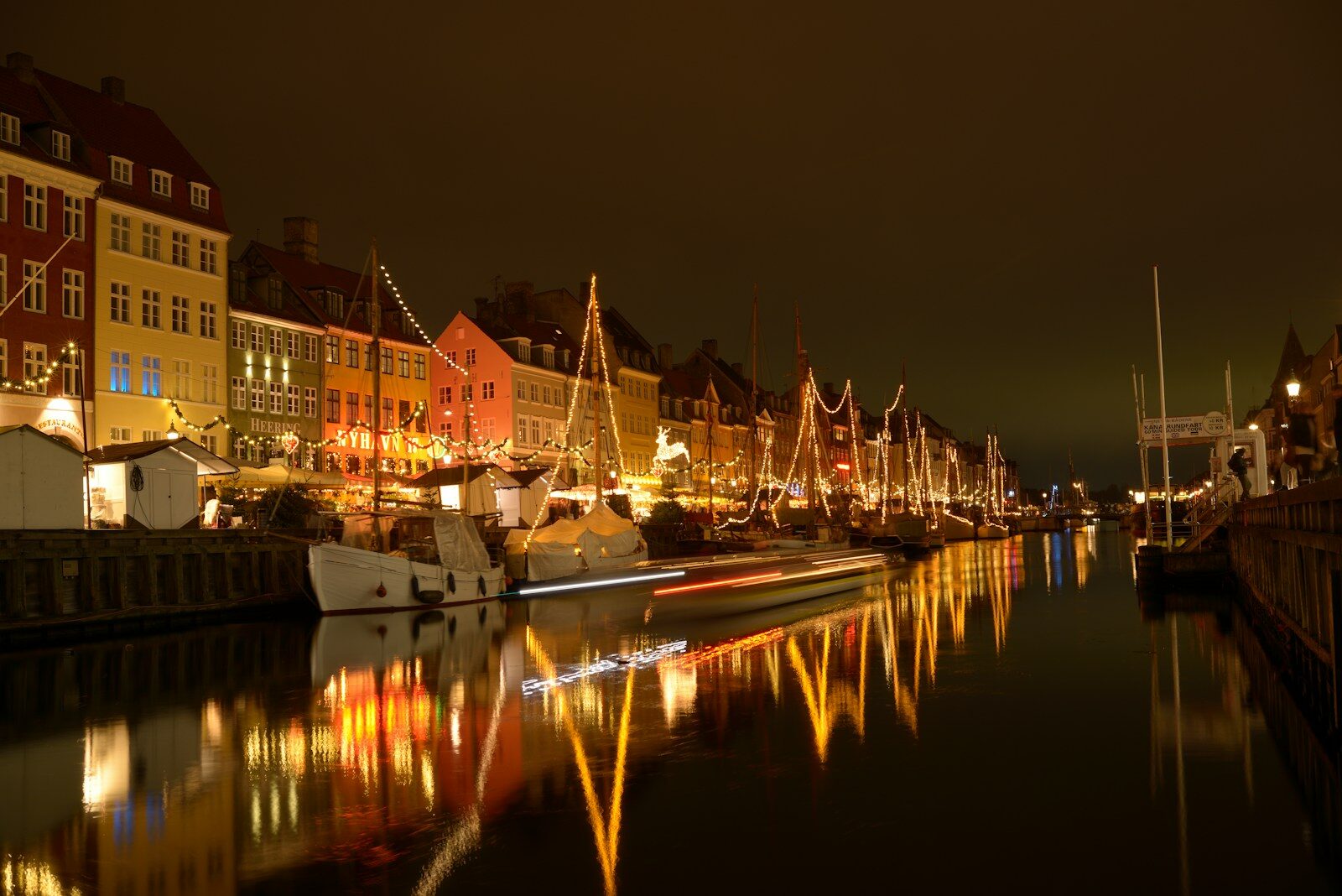 Nyhavns farvede huse og både med lyskæder spejler sig i kanalen om aftenen