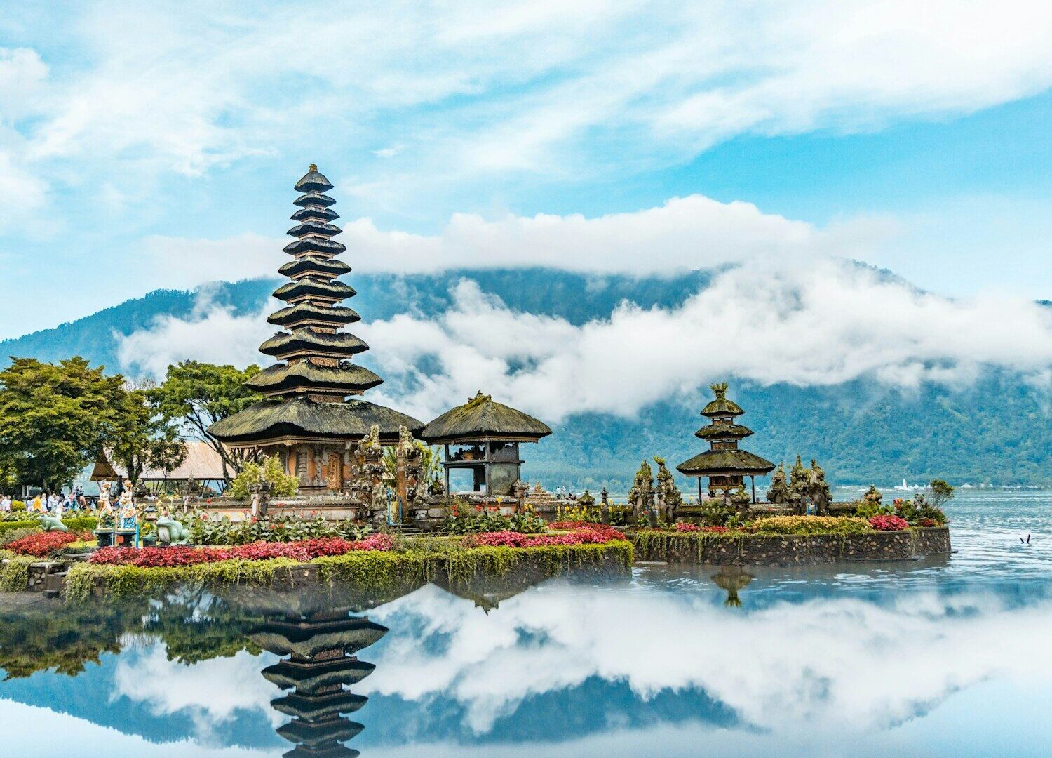 brown and green temple near body of water under blue and white cloudy sky during daytime