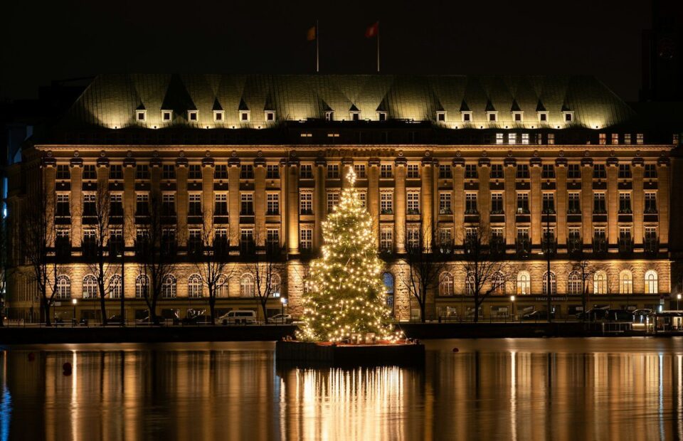 Oplyst juletræ på Binnenalster foran en oplyst bygning i Hamborg