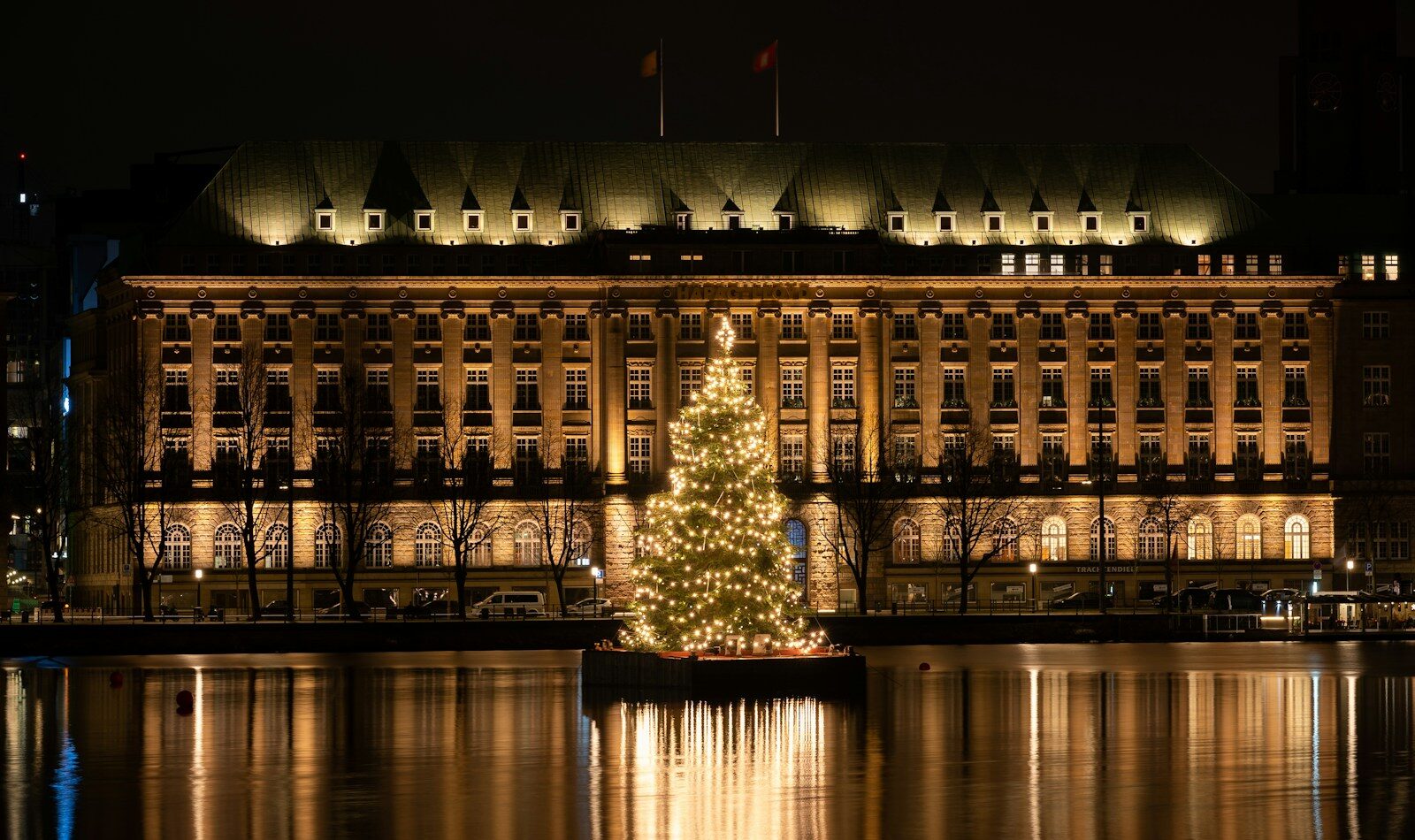 Oplyst juletræ på Binnenalster foran en oplyst bygning i Hamborg