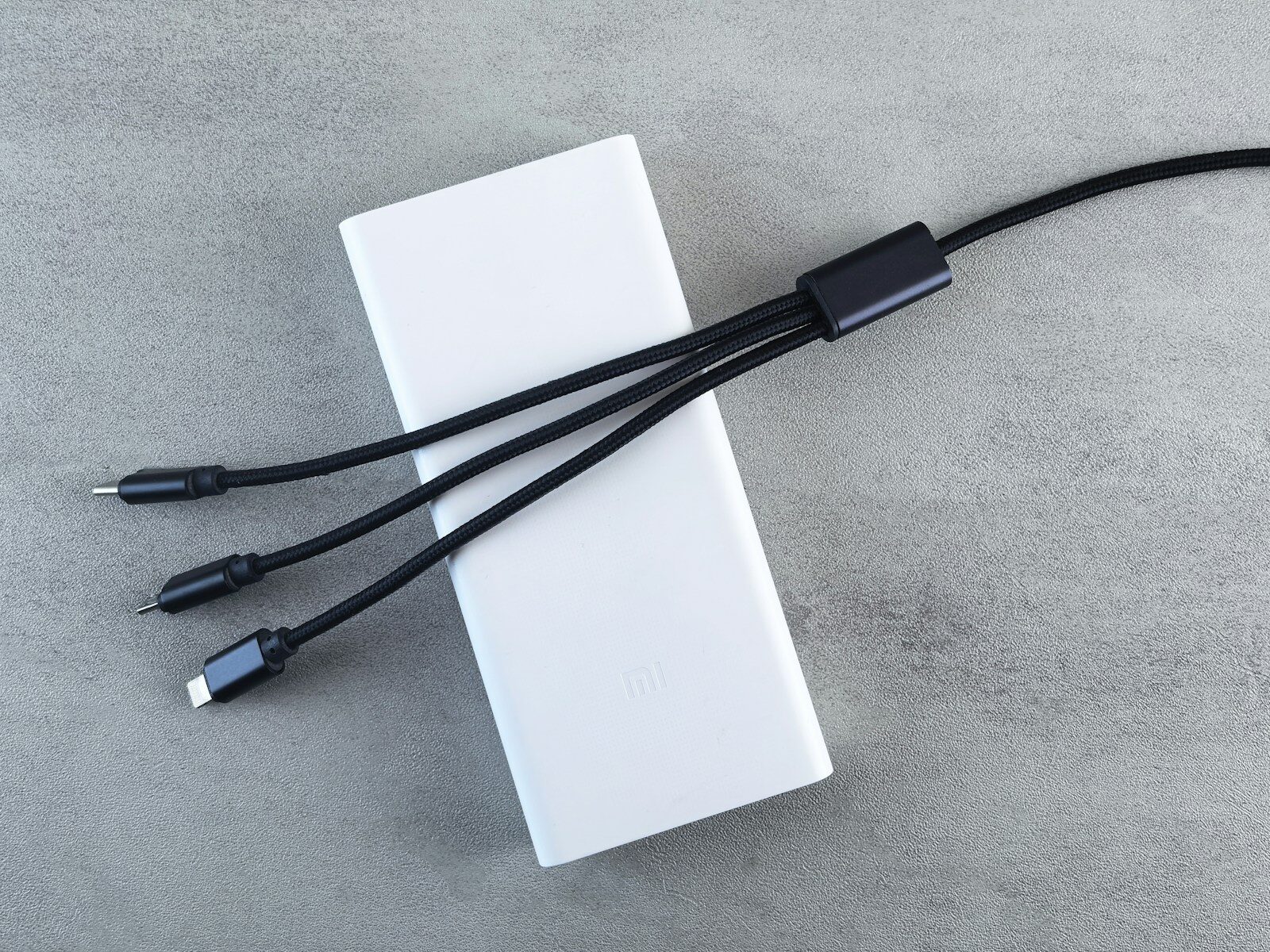 Hvid powerbank med tre sorte ladekabler på et lyst underlag