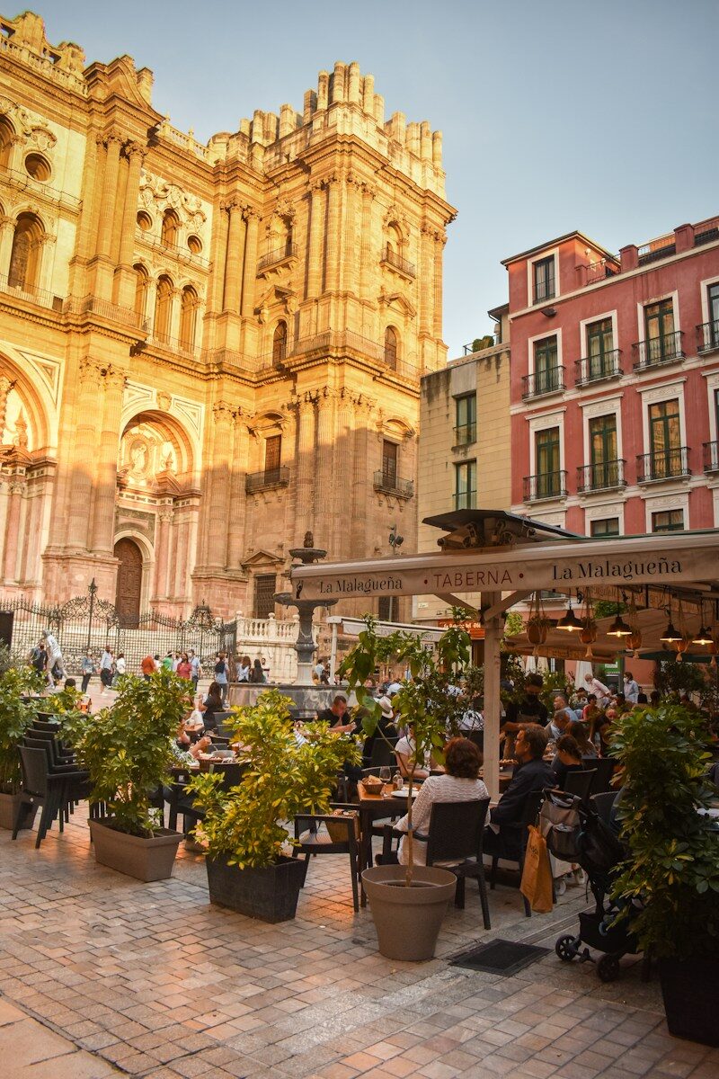 Cafébordene foran Málagas katedral med sol på den gyldne facade