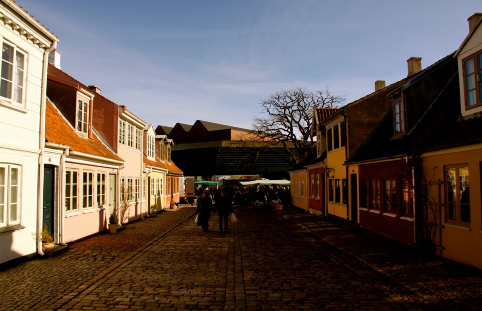 Sne langs en brostensgade med lave, farverige huse i Odense