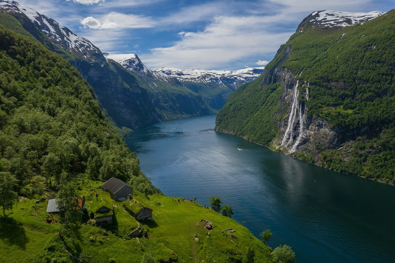 Geirangerfjorden mellem grønne fjeldsider med vandfald ned mod vandet