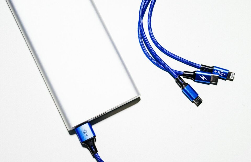 Lys powerbank med et blåt ladekabel og flere stik på hvid baggrund