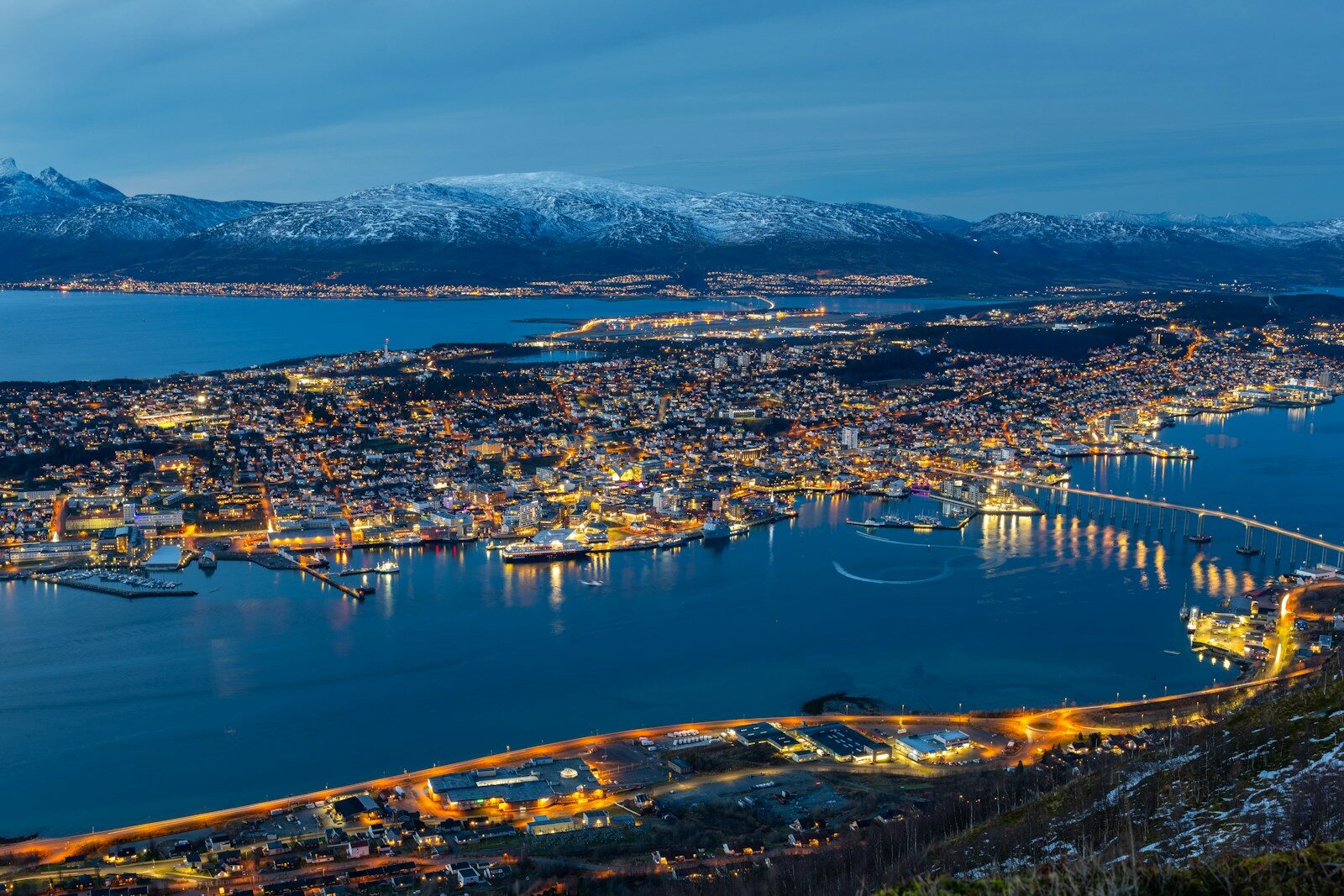 Udsigt over Tromsøs oplyste bymidte, bro og fjord ved aften i Norge